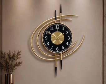 Op de afbeelding: Een wandklok met een ronde zwarte wijzerplaat, gouden cijfers en een centraal gouden zonnestraalontwerp. De klok is omlijst door gebogen gouden metalen bogen en twee verticale gouden staven met zwarte uiteinden boven en onder de klok.