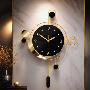Op de afbeelding: Een wandklok met een ronde zwarte wijzerplaat met goudkleurige wijzers en cijfers voor 3, 6, 9 en 12. De klok is omlijst door gouden metalen ringen en geometrische accenten, waaronder zwarte cirkelvormige elementen en een slinger.