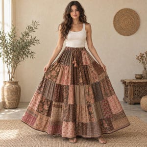 May include: A white sleeveless tank top paired with a floor-length, tiered maxi skirt featuring a patchwork design of various brown, tan, and muted pink floral and paisley patterns, finished with a drawstring waist and decorative tassels.