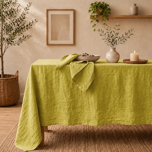 May include: A rectangular table covered with a solid lime green linen tablecloth. A matching folded linen napkin rests on top of the table. The fabric has a visible woven texture and drapes over the edges of the table, creating soft folds.