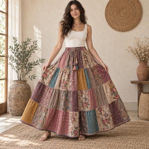 May include: A floor-length, tiered maxi skirt featuring a patchwork design with various floral, paisley, and striped patterns in shades of burgundy, mustard yellow, and teal. The skirt has an elasticated waistband with a drawstring and tassels.