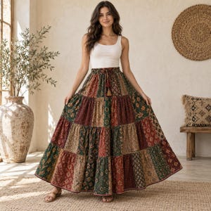 Könnte beinhalten: Ein langer, gestufter Maxirock mit Patchwork-Design, bestehend aus verschiedenen Blumen- und geometrischen Mustern in den Farben Dunkelrot, Waldgrün und Beige. Der Rock hat einen elastischen Bund mit Kordelzug und zwei hängenden Quasten.
