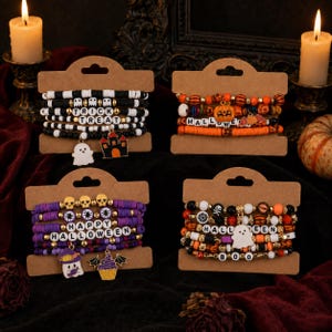 Puede incluir: Cuatro juegos de pulseras de cuentas en tarjetas de exhibición de cartón. Un juego presenta cuentas blancas y negras con un dije de fantasma y casa embrujada. Otro tiene cuentas naranjas con un dije de calabaza. Un tercero tiene cuentas moradas con dijes de fantasma y cupcake. El último juego incluye cuentas naranjas, negras y blancas con un dije de fantasma.