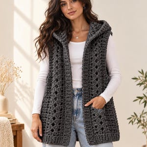 May include: A dark gray sleeveless hooded vest featuring an open front design with a textured crochet pattern, two front pockets, and a ribbed hem, worn over a plain white long-sleeve shirt and light blue denim jeans.