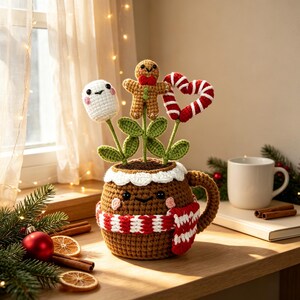 May include: A brown crocheted mug cozy featuring a smiling face and a red and white striped scarf. Inside the mug are three crocheted stems: a white marshmallow, a brown gingerbread person with a red bow, and a red and white heart shape.