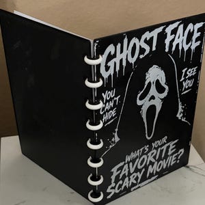 May include: A black notebook with white disc-bound rings featuring a white graphic of the Ghost Face mask. The cover includes the text GHOST FACE, YOU CAN'T HIDE, I SEE YOU, and WHAT'S YOUR FAVORITE SCARY MOVIE? in a stylized, dripping font.