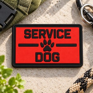 May include: A rectangular patch with a bright red background and a thick black border. The text SERVICE DOG is embossed in black, separated by a black horizontal line and a central black paw print icon. The patch has a bold, high-contrast design.