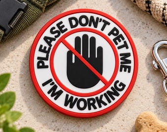 May include: A circular red, white, and black patch featuring a graphic of a black hand inside a red prohibition circle. The text reads PLEASE DON'T PET ME I'M WORKING in bold black capital letters arranged around the central hand icon.