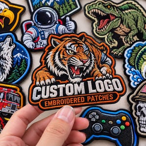May include: A collection of embroidered patches featuring various designs including a tiger, a wolf, a dinosaur, an astronaut, a fire truck, a skull in a helmet, and a game controller. One patch in the center displays the text CUSTOM LOGO EMBROIDERED PATCHES.