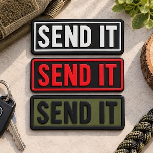 May include: Three rectangular morale patches featuring the text SEND IT in raised lettering. The top patch is black with white text, the middle is black with red text, and the bottom is olive green with black text, all with a black border.