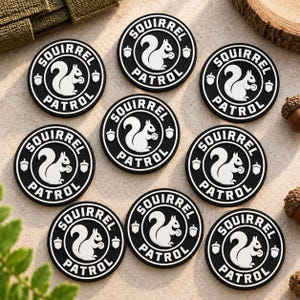 May include: Eight circular black and white patches featuring a central white squirrel graphic holding an acorn, surrounded by the text SQUIRREL PATROL and two small acorn icons. The patches have a raised, molded design with a clean, bold aesthetic.