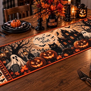 May include: A rectangular Halloween table runner featuring a printed scene of a haunted house, ghosts, jack-o'-lanterns, a black cat, and bats under a full moon. The text Trick or Treat is centered on the runner, which has an orange border.