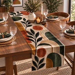 May include: A velvet table runner featuring a cream background with a printed pattern of dark green leaves, burnt orange circles, and gold arched lines. The fabric has a soft texture and is laid flat across a wooden dining table with place settings.