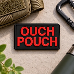 May include: A rectangular black patch with raised red lettering that reads OUCH POUCH. The patch features a clean, bold font and a smooth, matte finish, designed for attachment to gear or accessories, presented as a standalone item.