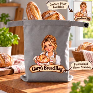 May include: A gray fabric bread bag featuring a graphic of a person holding a loaf of bread with the text Gary's Bread Bag. The bag has a top flap with a black button closure. Text on the image includes Custom Photo Available and Personalized Name Available.