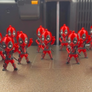 Puede incluir: Una colección de once pequeñas figuras estilizadas que representan a un personaje con traje rojo y negro, parches oculares blancos y cabeza redonda. Cada figura se muestra en una pose dinámica, algunas con las manos levantadas.