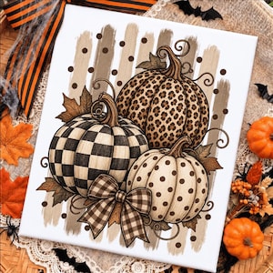 Peut inclure: Une impression sur toile rectangulaire représentant trois citrouilles aux motifs distincts : un motif à carreaux noir et blanc, un motif léopard marron et un motif à pois marron. Un nœud à carreaux marron est placé devant les citrouilles.