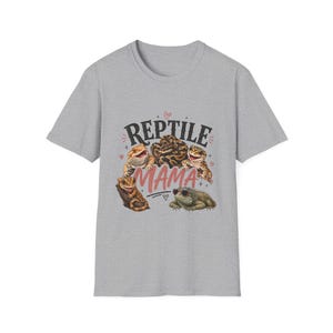 Op de afbeelding: Een grijs gemêleerd T-shirt met korte mouwen en een grafische print van diverse reptielen, waaronder een baardagame, een slang, een gekko en een leguaan met een zonnebril. De tekst REPTILE MAMA is in zwart en roze met kleine hartjes gedrukt.
