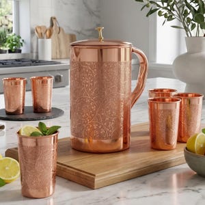 Puede incluir: Una jarra de cobre y cinco vasos a juego, cada uno con un intrincado patrón floral en relieve. La jarra tiene una tapa con un pequeño pomo y un asa lateral curva. Los vasos son cilíndricos y presentan un acabado de cobre pulido.
