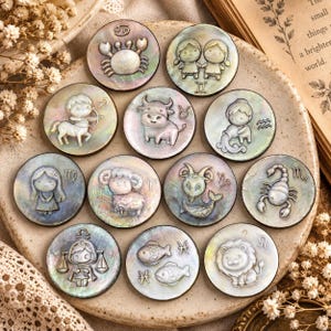 May include: A collection of twelve circular iridescent mother-of-pearl tokens, each featuring a raised relief carving of a different zodiac sign, including Cancer, Gemini, Sagittarius, Taurus, Aquarius, Virgo, Aries, Capricorn, Scorpio, Libra, Pisces, and Leo.
