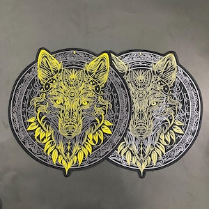 May include: Two circular patches featuring a stylized wolf head design. The wolf is rendered in bright yellow and white line art against a black background, surrounded by intricate geometric patterns and circular borders with fine detailing.