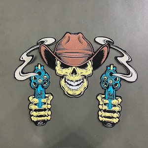 May include: An embroidered patch featuring a central skull wearing a brown cowboy hat, flanked by two skeletal hands each holding a blue revolver with white smoke trails rising from the barrels, all outlined in black thread on a dark background.