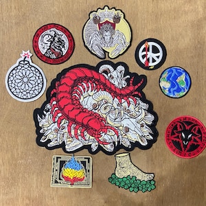 May include: A collection of embroidered patches featuring a large red centipede on a pile of skulls, a goat head in a red circle, a crowned figure, a bomb, a peace sign with an arrow, a globe, a pentagram goat, a burning book, and a foot on leaves.