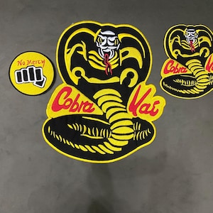 May include: Three embroidered patches featuring a black and yellow cobra snake design with the red text Cobra Kai, a smaller version of the same cobra design, and a circular patch with a black fist graphic and the red text No Mercy.