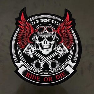 May include: A circular embroidered patch featuring a white skull wearing a helmet and goggles, flanked by red wings. Two crossed engine pistons are positioned below the skull. A banner at the bottom displays the red text RIDE OR DIE.