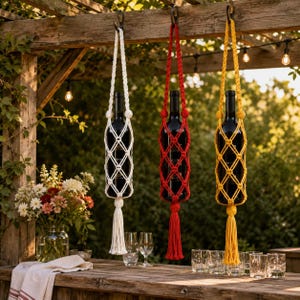 May include: Three glass wine bottles suspended in macrame holders. The holders are made of braided cord in white, red, and yellow, each featuring a diamond-patterned net design and a long tassel at the bottom, hanging from a wooden structure.