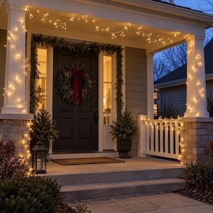 May include: A front porch decorated for the holidays with warm white string lights wrapped around white columns and railings. A dark door features a green pine wreath with a large red velvet bow, flanked by two potted evergreen trees and a black lantern.