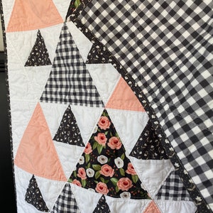 May include: A quilt with a black and white gingham pattern, peach pink triangles, and floral fabric triangles. The quilt is made with a variety of fabrics and patterns.