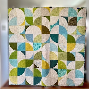 May include: A quilt with a geometric pattern of green, blue, yellow, and white half circles. The quilt is made with different fabrics and has a white background.