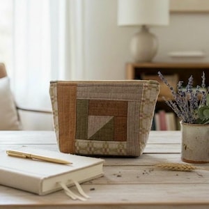 May include: A rectangular zippered pouch featuring a patchwork design with fabric panels in shades of olive green, brown, and beige. The exterior displays a geometric pattern with stitched details, constructed from textured fabric with a top zipper closure.
