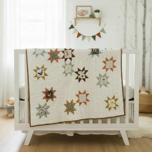May include: A white baby crib with a star-patterned quilt. The quilt features various star shapes in shades of brown, orange, and green, with animal and floral patterns. The crib is set against a backdrop of a light-colored wall and a window.