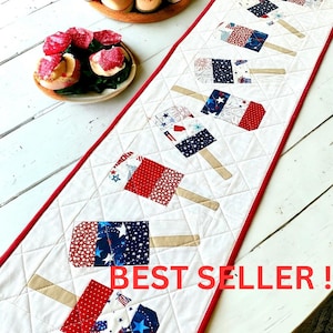 May include: A white quilted table runner with a red border, featuring patriotic popsicle designs in red, white, and blue fabrics. The text "BEST SELLER!" is displayed in red.