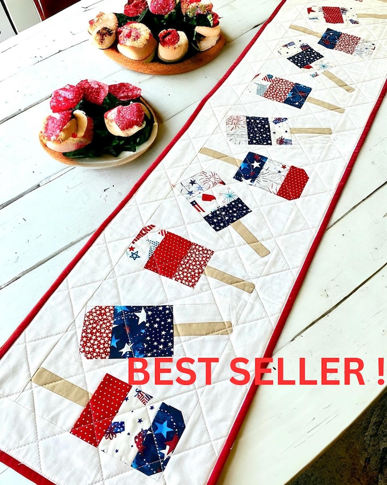 May include: A white quilted table runner with a red border, featuring patriotic popsicle designs in red, white, and blue fabrics. The text "BEST SELLER!" is displayed in red.