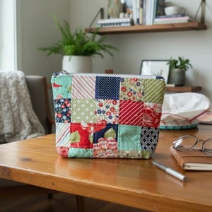 May include: A rectangular zippered pouch constructed from a patchwork of various fabric squares featuring floral, polka dot, striped, and geometric patterns in shades of red, green, blue, and white, with a silver-toned metal zipper closure at the top.