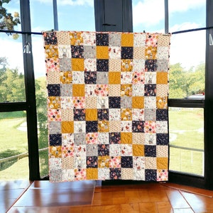 May include: A patchwork quilt with a variety of fabrics in shades of yellow, white, black, and pink. The quilt is made up of squares with different patterns and designs, including stars, animals, and geometric shapes.