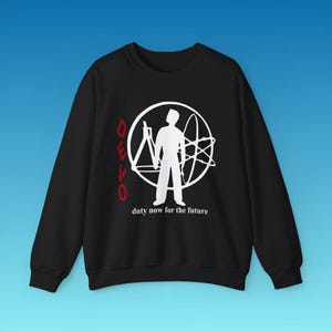 May include: A black long-sleeve sweatshirt featuring a white graphic of a person standing inside a circle with scientific symbols. The word DEVO is printed in red vertically on the left, and the text duty now for the future is in white below.