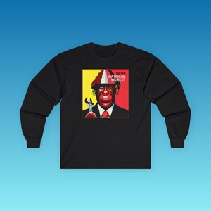 May include: A black long-sleeve shirt featuring a graphic print of a chimpanzee wearing a red and white tiered hat, a suit, and a red tie. The chimpanzee holds a silver wrench. The text DEVO WATCH US WORK IT is printed in the upper right corner.