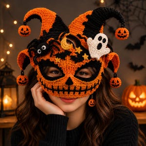 May include: A crocheted jester-style mask in orange and black, featuring dangling miniature jack-o'-lanterns, a white ghost appliqué, a black spider, a yellow crescent moon, and small yellow stars, with a stitched mouth and eye openings.