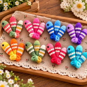 May include: Eight sets of three small, crocheted fish-shaped ornaments arranged in two rows. Each fish features horizontal stripes in various colours including pink, green, blue, purple, yellow, and orange, with a single black bead for an eye.
