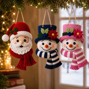 Könnte beinhalten: Drei gehäkelte Weihnachtsanhänger, die an Schnüren hängen. Einer ist ein Weihnachtsmann mit roter Mütze und weißem Bart. Die anderen beiden sind Schneemänner, einer mit blauem Zylinder und blauem Schal, der andere mit rosa Zylinder und Schal.