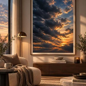 May include: A large rectangular framed wall art print depicting a dramatic sunset with dark clouds and golden light rays. The artwork is displayed on a neutral wall above a long wooden media console in a living room setting with furniture.