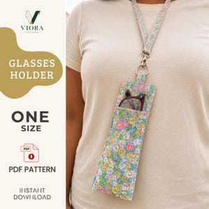 Puede incluir: Un estuche para gafas de tela con estampado floral y un cordón para el cuello a juego. El estuche presenta un patrón vibrante de pequeñas flores rosas, amarillas y azules sobre un fondo claro. Unas gafas de montura oscura están dentro.
