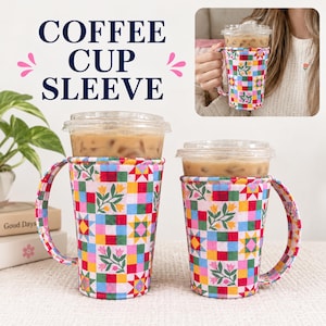 Puede incluir: Dos fundas de tela para vasos de café con asas, con un colorido patrón de patchwork de cuadrados, motivos de estrellas amarillas y diseños de tulipanes rosas. Cada funda rodea un vaso de plástico transparente con café helado y textura acolchada.