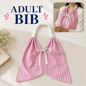 May include: An adult bib featuring a pink and white vertical striped pattern. The bib has a white fabric neck loop and a white ribbon tie closure at the center front. The text ADULT BIB is printed in dark blue above the product.