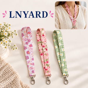 May include: Three fabric lanyards with metal swivel clasps. One features a white background with pink and purple flowers, one has a pink background with strawberries and small white flowers, and one has a green gingham pattern with white daisies.