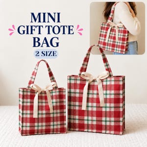 May include: Two rectangular tote bags featuring a red, white, and green plaid pattern with a cream-colored ribbon bow tied at the top center. The text "MINI GIFT TOTE BAG 2 SIZE" is printed in dark blue with pink decorative accents above the bags.